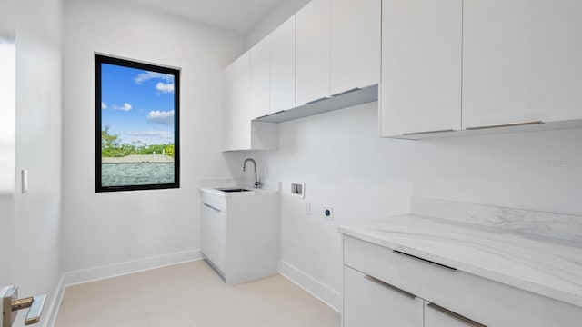 clothes washing area with cabinet space, baseboards, hookup for a washing machine, hookup for an electric dryer, and a sink