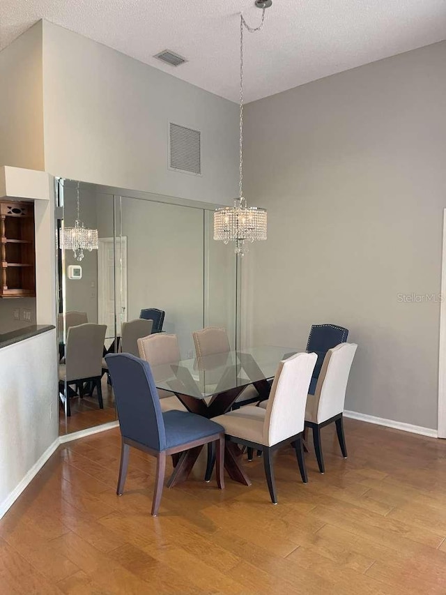 dining room featuring a towering ceiling, hardwood / wood-style floors, a textured ceiling, and an inviting chandelier