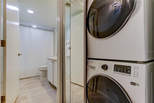 laundry room featuring stacked washer / drying machine and light hardwood / wood-style floors