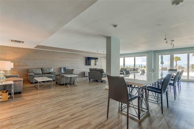 dining space featuring a healthy amount of sunlight, light hardwood / wood-style floors, and wood walls