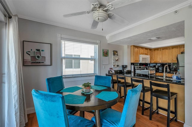 dining room featuring ornamental molding, visible vents, ceiling fan, and wood finished floors