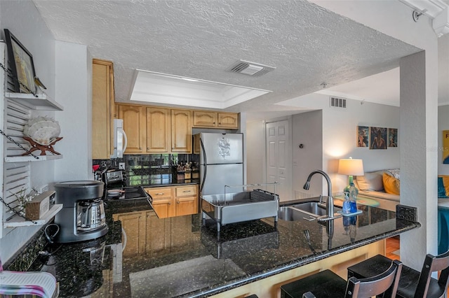 kitchen featuring visible vents, dark stone countertops, freestanding refrigerator, a peninsula, and a sink