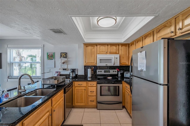 kitchen featuring stainless steel appliances, a sink, visible vents, dark stone counters, and a raised ceiling