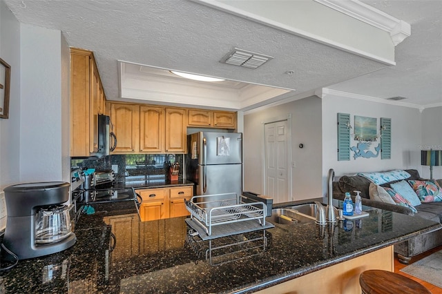 kitchen with dark stone countertops, a tray ceiling, appliances with stainless steel finishes, and a peninsula