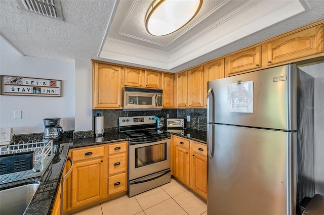 kitchen featuring stainless steel appliances, a tray ceiling, visible vents, and dark stone counters