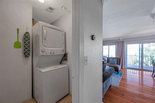 washroom featuring a textured ceiling, a textured wall, stacked washer and dryer, laundry area, and light wood-type flooring