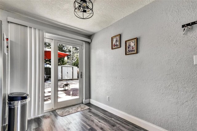 doorway to outside with dark wood-style floors, baseboards, a textured ceiling, and a textured wall