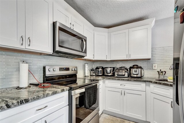 kitchen with appliances with stainless steel finishes, white cabinets, and backsplash