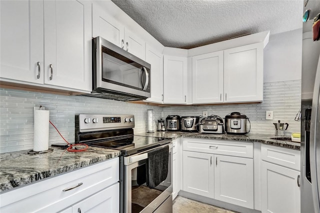 kitchen featuring stainless steel appliances, white cabinetry, decorative backsplash, and dark stone countertops