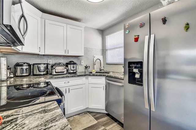 kitchen featuring stainless steel appliances, a sink, light wood-style floors, white cabinets, and dark stone counters