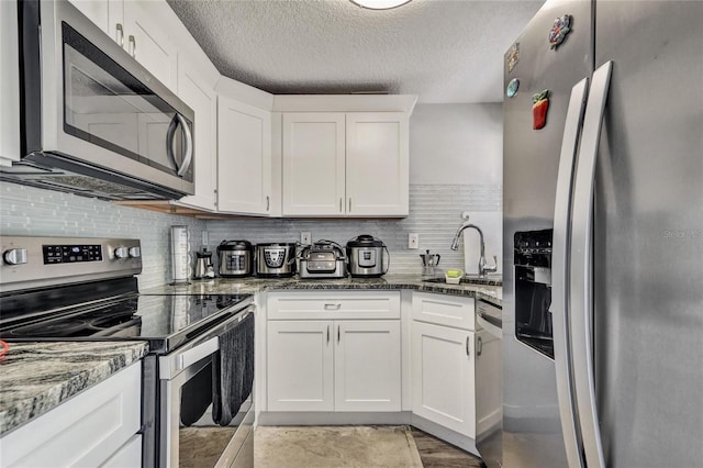 kitchen featuring white cabinets, backsplash, dark stone counters, and appliances with stainless steel finishes