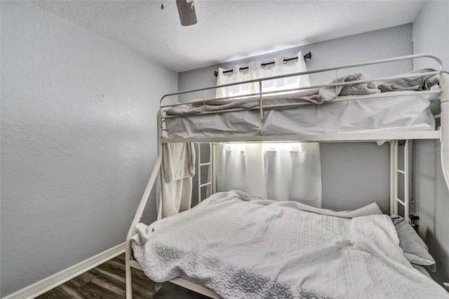 bedroom with a textured ceiling, a textured wall, dark wood-style flooring, a ceiling fan, and baseboards