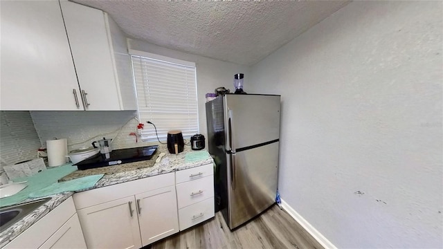 kitchen with light wood finished floors, white cabinets, freestanding refrigerator, light stone countertops, and backsplash