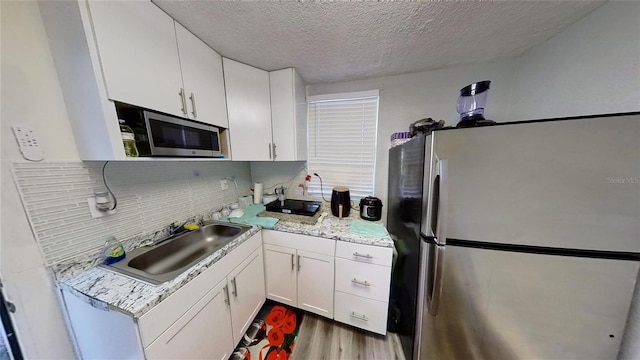 kitchen with decorative backsplash, wood finished floors, stainless steel appliances, white cabinetry, and a sink