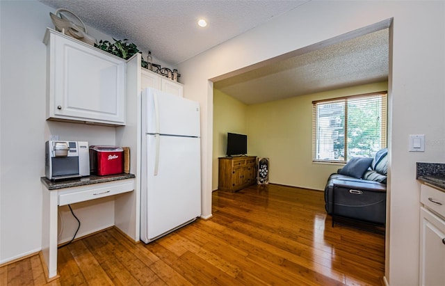 kitchen with a textured ceiling, wood-type flooring, white refrigerator, and white cabinets