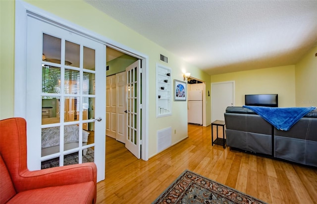 living room with built in features, a textured ceiling, french doors, and hardwood / wood-style floors