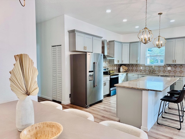 kitchen with decorative light fixtures, wall chimney range hood, light hardwood / wood-style floors, a kitchen island, and appliances with stainless steel finishes