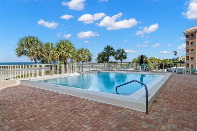 community pool featuring a patio area, a water view, and fence