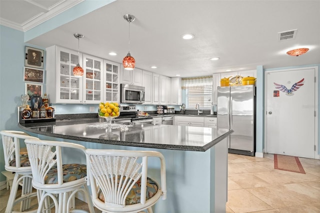 kitchen with kitchen peninsula, stainless steel appliances, pendant lighting, white cabinetry, and a breakfast bar area