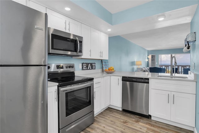 kitchen with appliances with stainless steel finishes, white cabinetry, sink, light hardwood / wood-style floors, and kitchen peninsula