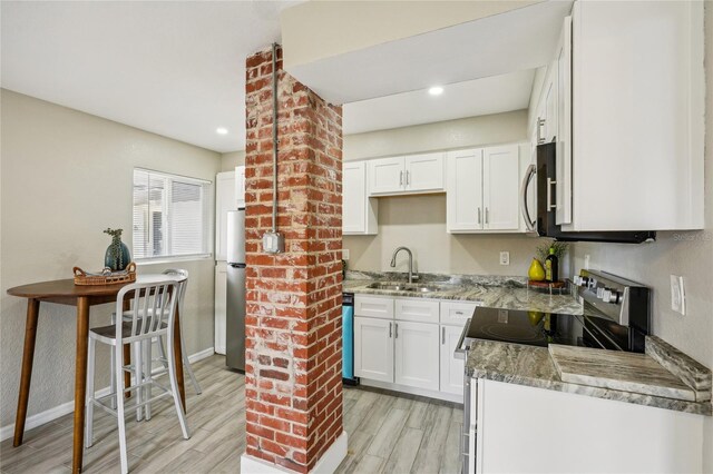 kitchen with sink, appliances with stainless steel finishes, light stone counters, white cabinets, and light wood-type flooring