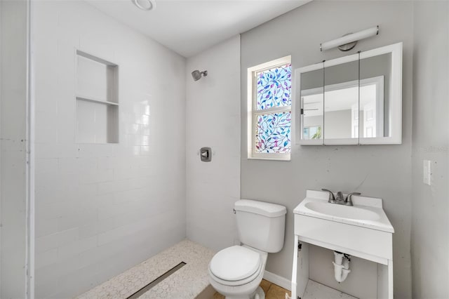 bathroom with sink, a tile shower, and toilet