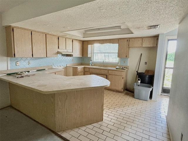 kitchen with sink, light brown cabinets, kitchen peninsula, decorative backsplash, and a textured ceiling