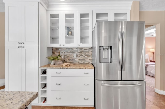 kitchen featuring stainless steel fridge, backsplash, white cabinetry, light stone counters, and light tile patterned flooring