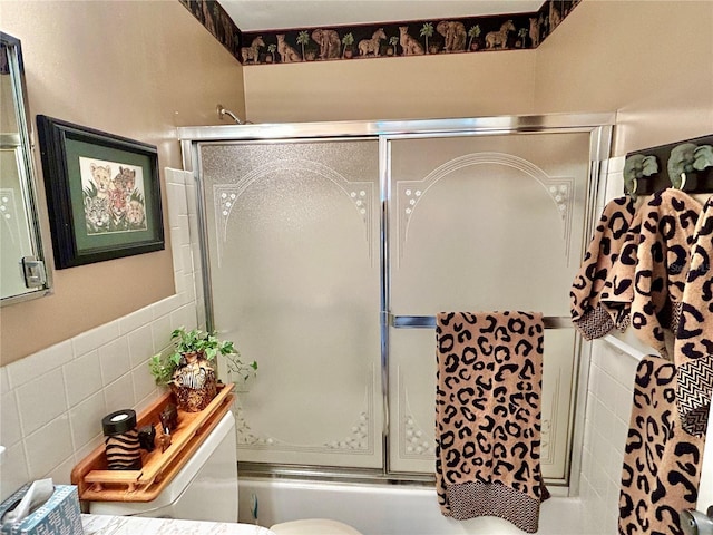 bathroom with enclosed tub / shower combo, toilet, and tile walls