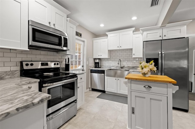 kitchen with white cabinets, stainless steel appliances, light stone countertops, and decorative backsplash