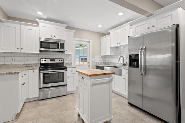 kitchen featuring white cabinets, appliances with stainless steel finishes, a kitchen island, wood counters, and tasteful backsplash