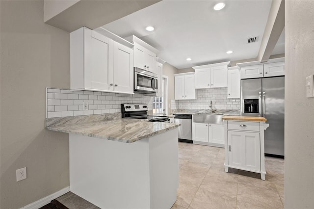 kitchen with appliances with stainless steel finishes, white cabinetry, sink, backsplash, and kitchen peninsula