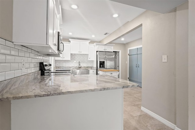 kitchen featuring white cabinets, stainless steel appliances, tasteful backsplash, kitchen peninsula, and light stone counters