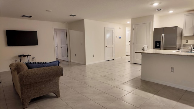 kitchen with light tile patterned floors, stainless steel fridge, sink, and white cabinets