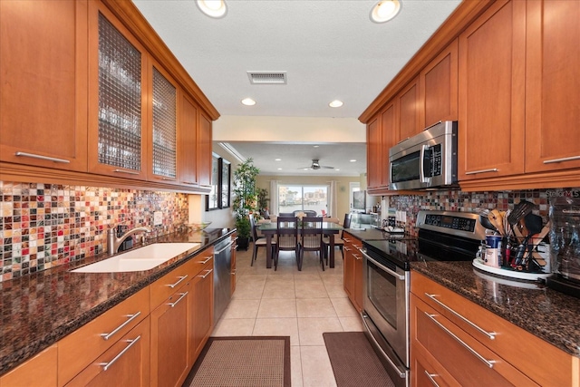 kitchen featuring sink, dark stone countertops, decorative backsplash, light tile patterned floors, and stainless steel appliances