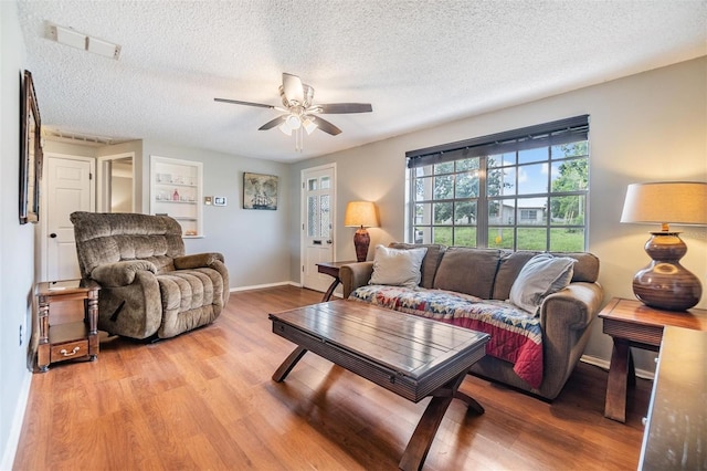 living room featuring ceiling fan, hardwood / wood-style flooring, built in features, and a textured ceiling