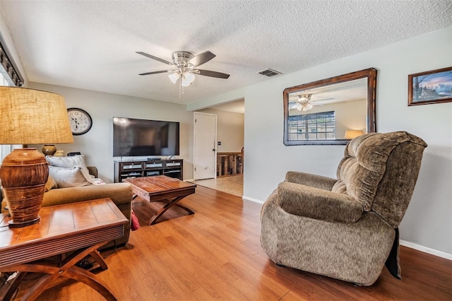 living room featuring light hardwood / wood-style floors, a textured ceiling, and ceiling fan