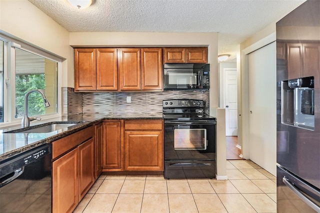 kitchen with light tile patterned floors, dark stone counters, backsplash, black appliances, and sink