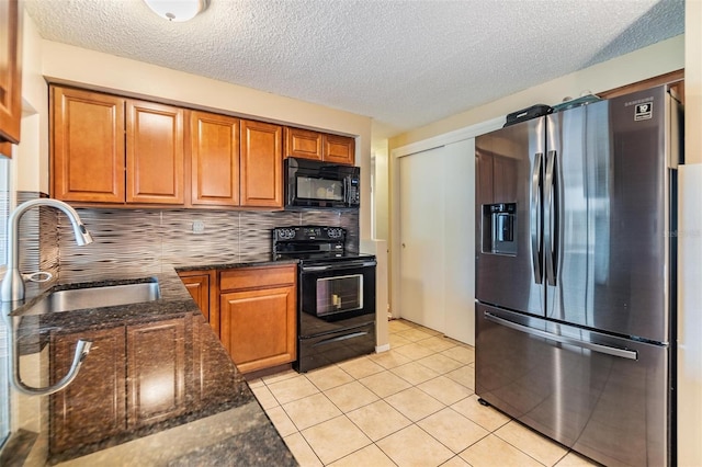 kitchen featuring dark stone counters, black appliances, sink, light tile patterned floors, and decorative backsplash