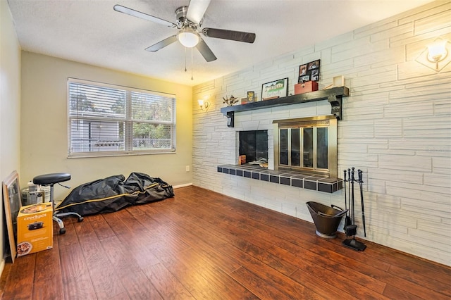 exercise room featuring a stone fireplace, a textured ceiling, ceiling fan, and hardwood / wood-style floors