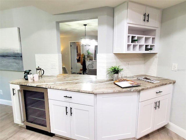 kitchen featuring pendant lighting, white cabinets, beverage cooler, light stone counters, and light wood-type flooring