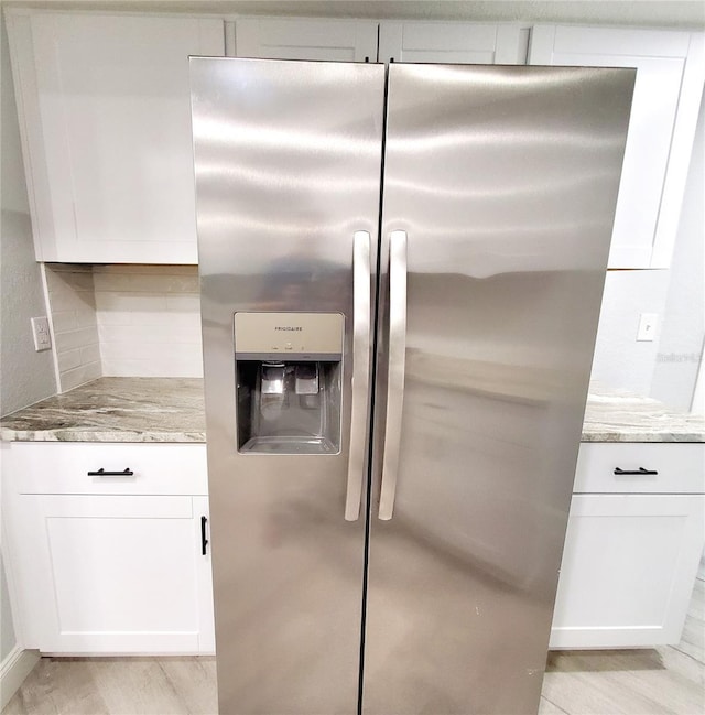 kitchen with stainless steel refrigerator with ice dispenser, light stone countertops, white cabinets, and light wood-type flooring