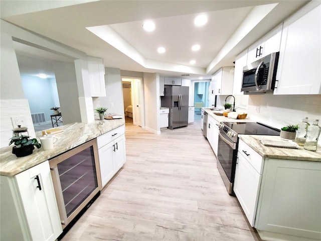 kitchen with white cabinets, beverage cooler, a raised ceiling, and appliances with stainless steel finishes