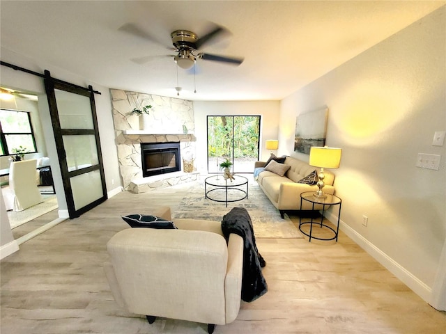 living room with ceiling fan, a fireplace, a barn door, and light hardwood / wood-style flooring