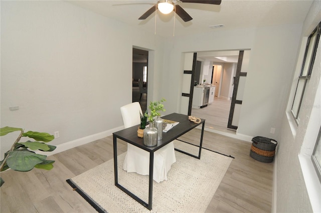 home office with light wood-type flooring, baseboards, visible vents, and ceiling fan