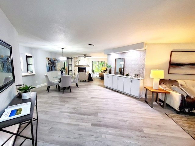 living room featuring light wood-type flooring, visible vents, a fireplace, and baseboards