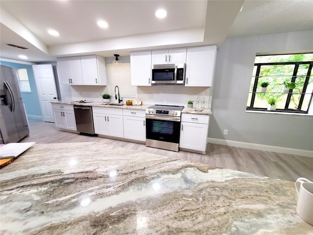 kitchen with stainless steel appliances, light wood-style floors, white cabinets, a sink, and baseboards