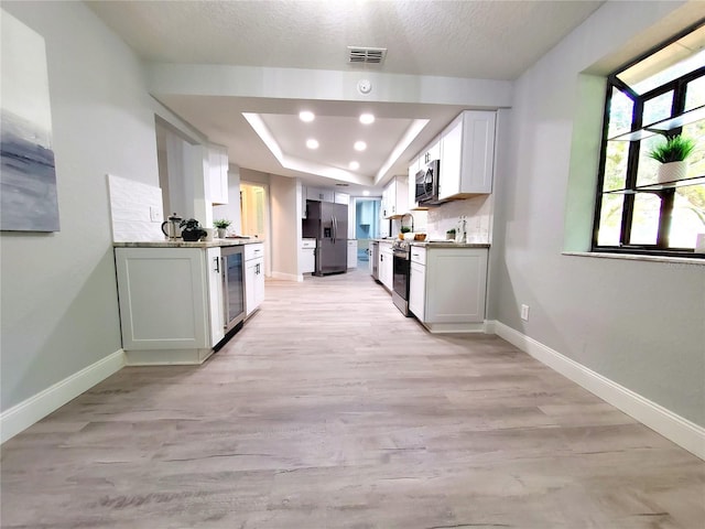 kitchen featuring stainless steel appliances, a tray ceiling, beverage cooler, and baseboards