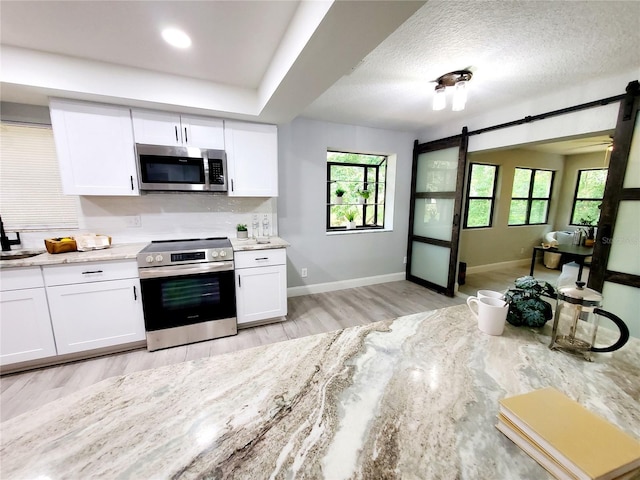 kitchen featuring stainless steel appliances, a barn door, decorative backsplash, and white cabinets