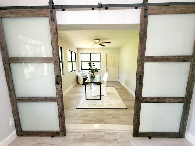 interior space featuring a ceiling fan, a barn door, baseboards, and wood finished floors